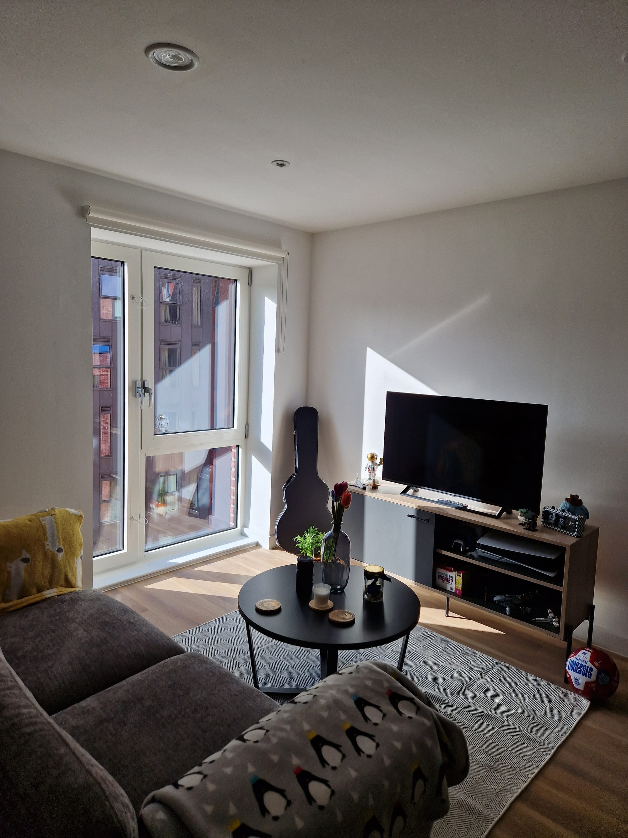 A small living room, with TV, sofa, and decorations. The sun lights the room through the window.